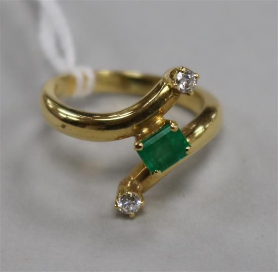 A modern 18ct gold and three stone emerald and diamond stylised crossover ring, size O.